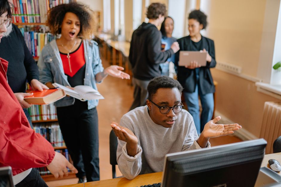 A diverse group of students collaborates around a tablet and laptops in a modern, professional setting, showcasing teamwork and digital literacy.