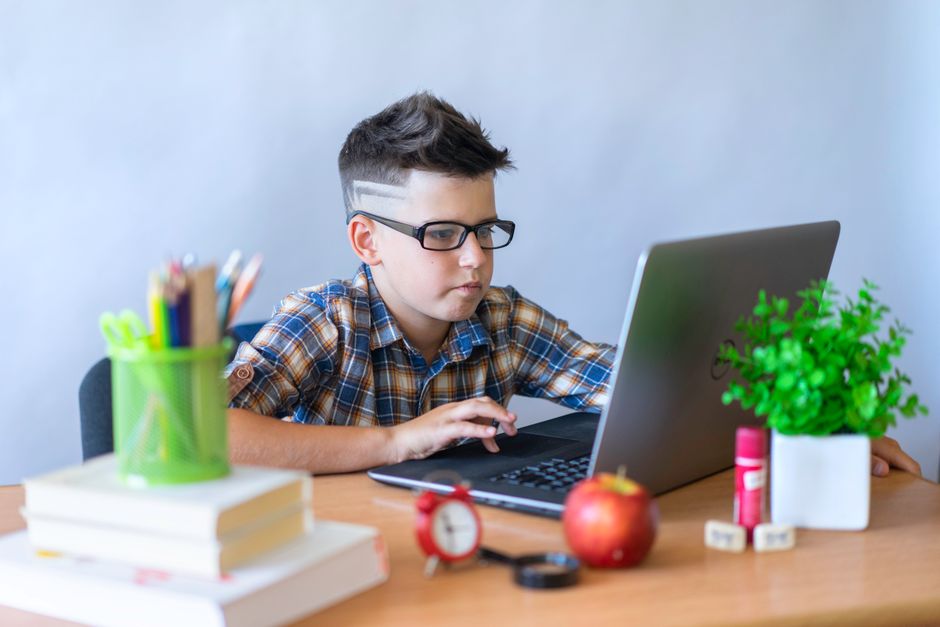 Focused young student works diligently on a laptop in a bright, modern classroom, representing the future of education and...