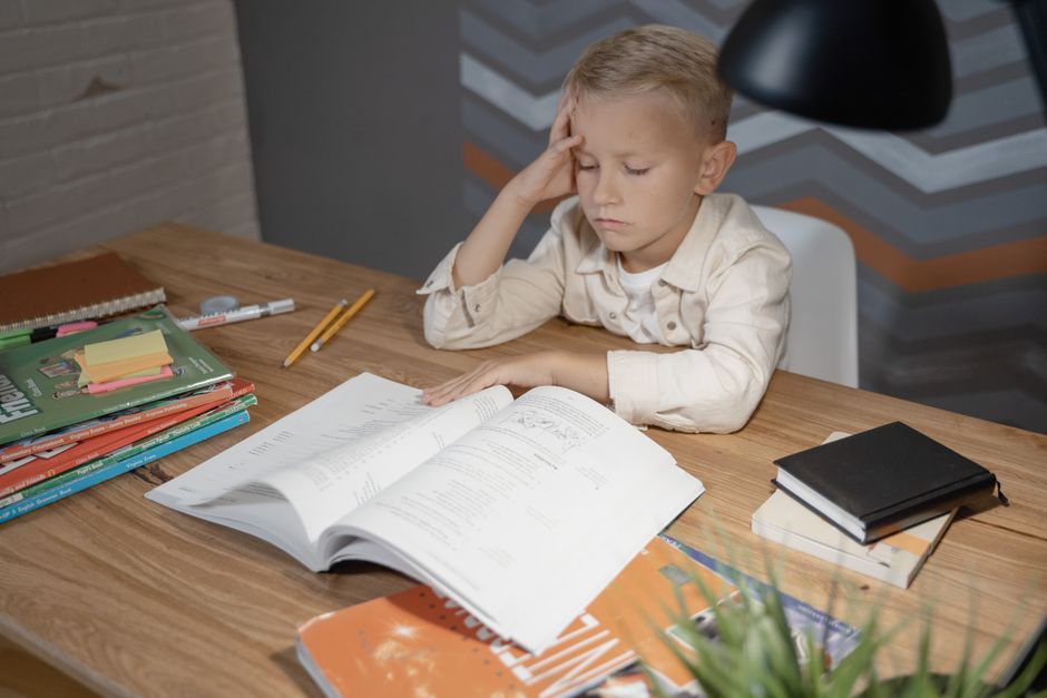 A young child sits at a wooden desk in their sunlit bedroom, focused on reading a book, representing the goal of a bright educational future.
